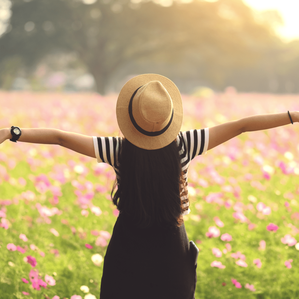 Frau mit Hut steht mitten auf einer Blumenwiese